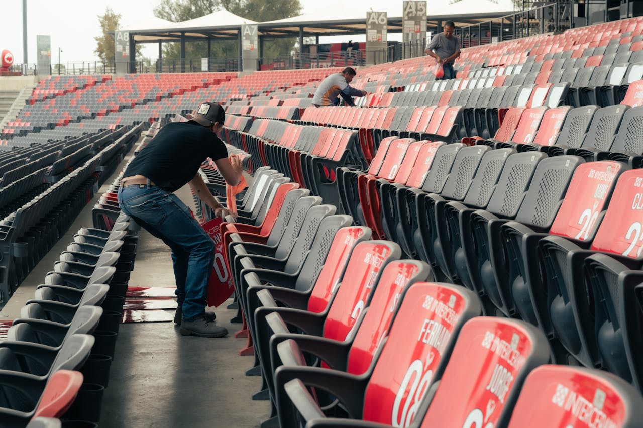 Event staff organizing stadium seating for an upcoming sports event with empty grandstands.